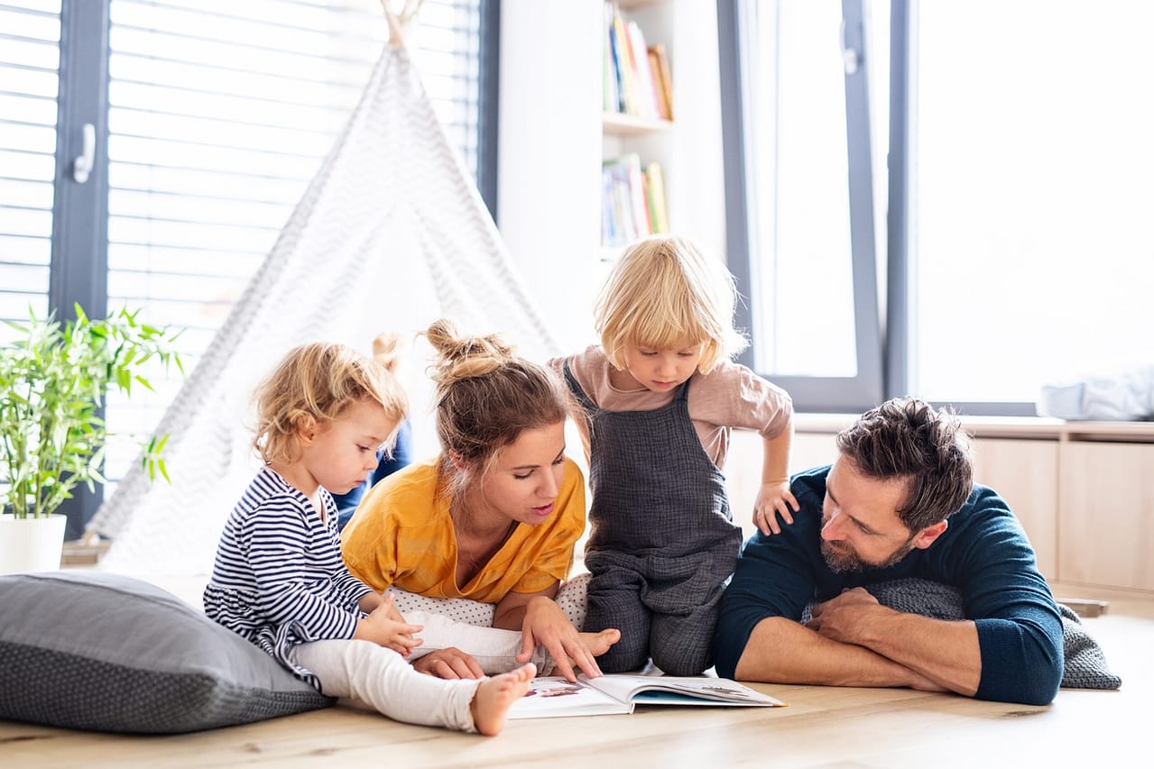junge familie mit zwei kindern ist im wohnzimmer und liest ein buch lebensidealisten neumuenster