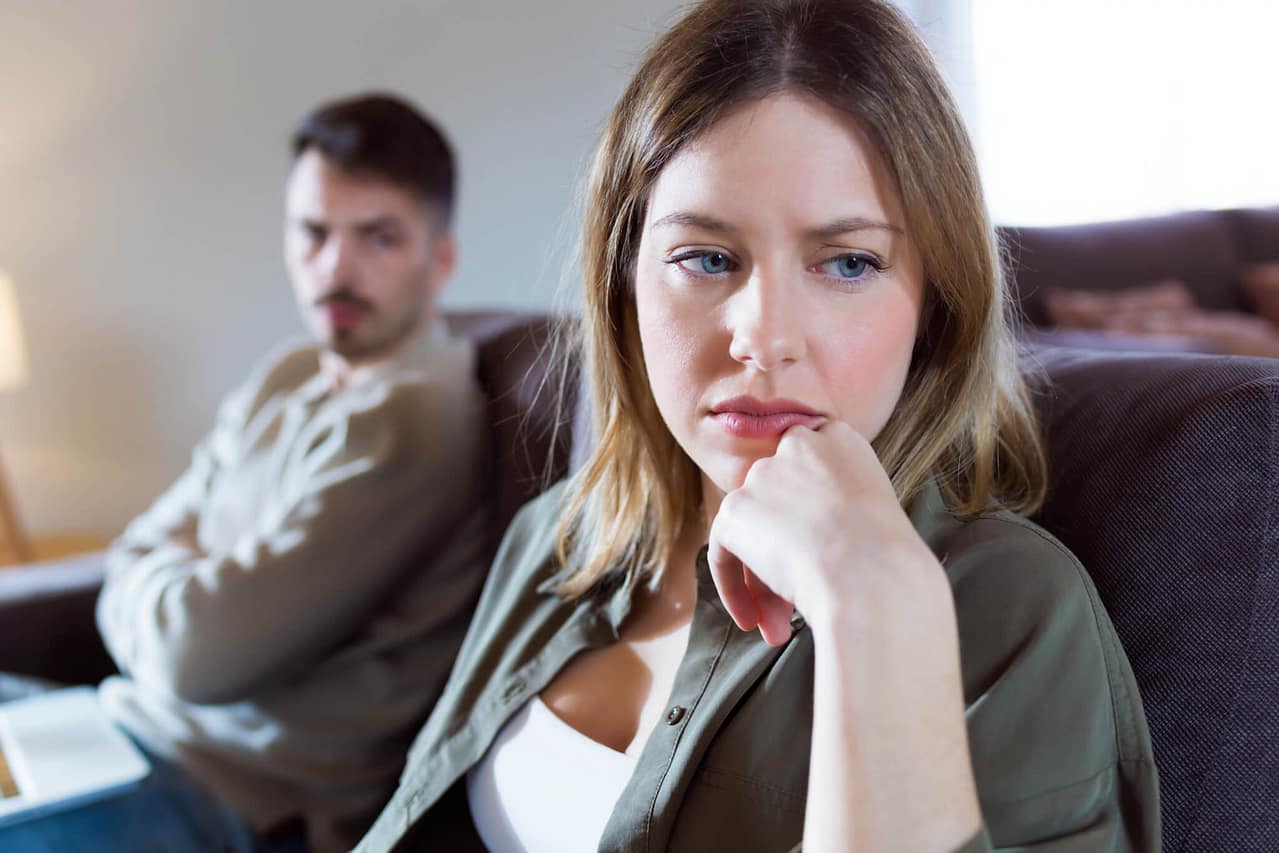 offended young woman ignoring her angry partner sitting behind her on the couch at home