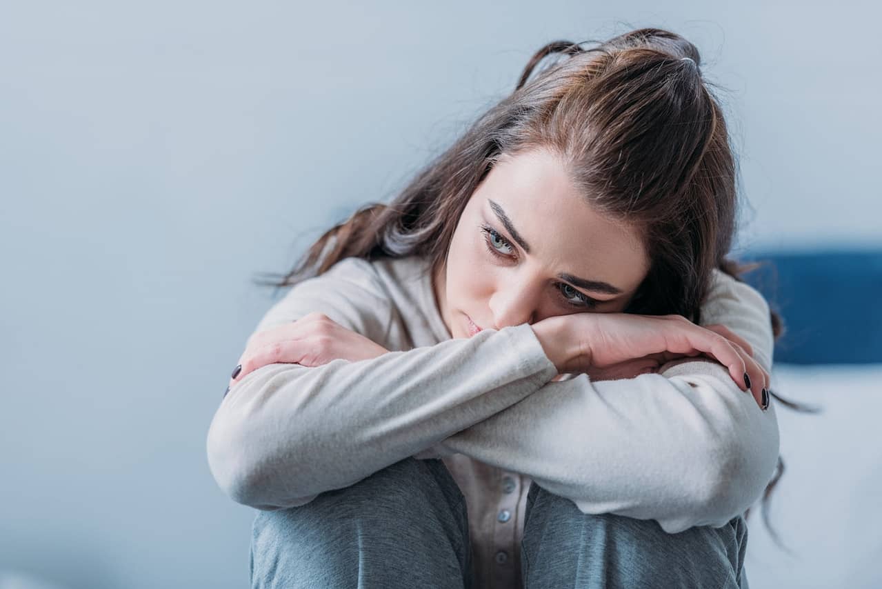 Bindungsangst überwinden: Symptome, Folgen und Lösungsstrategien 2 frau sitzt zusammengekauert auf dem bett und guckt traurig in die ferne