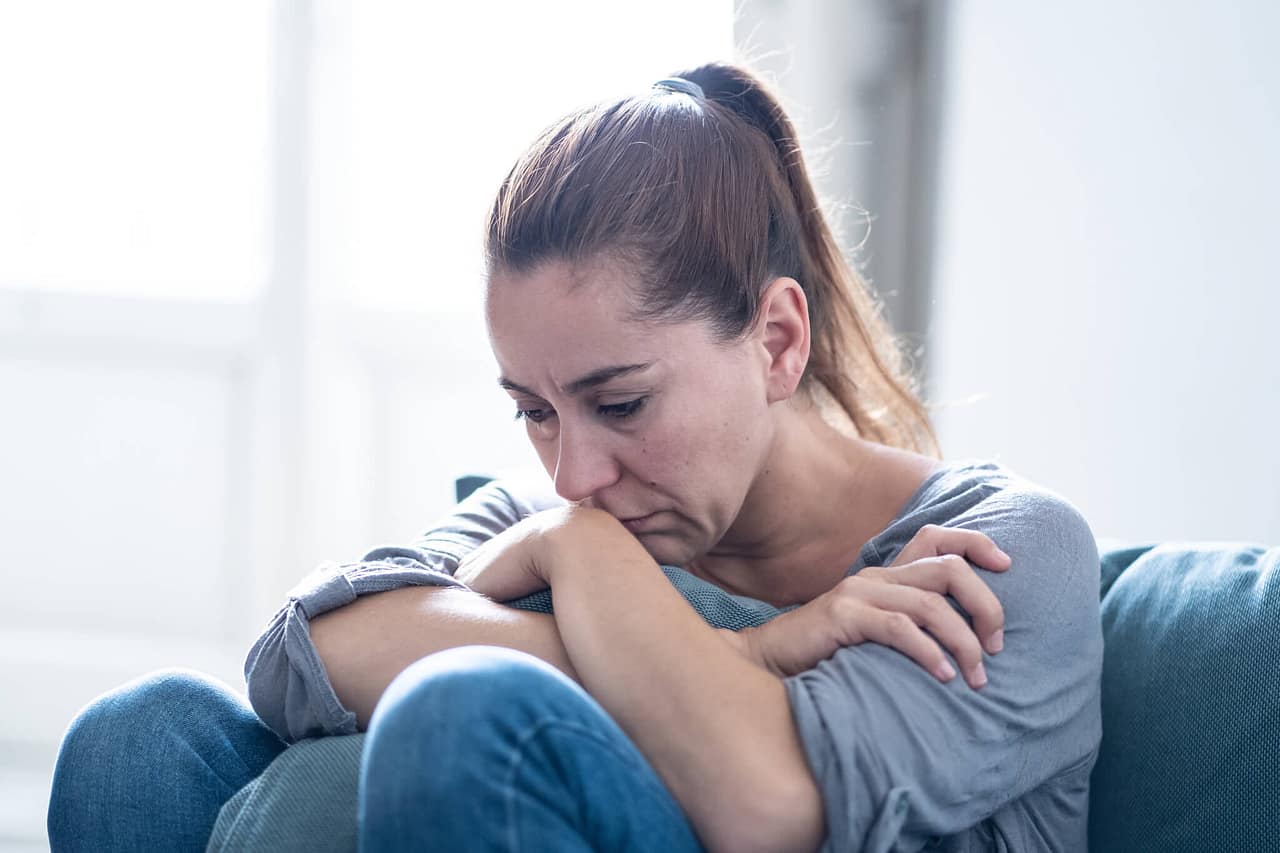 Braunhaarige Frau sitzt traurig im Wohnzimmer