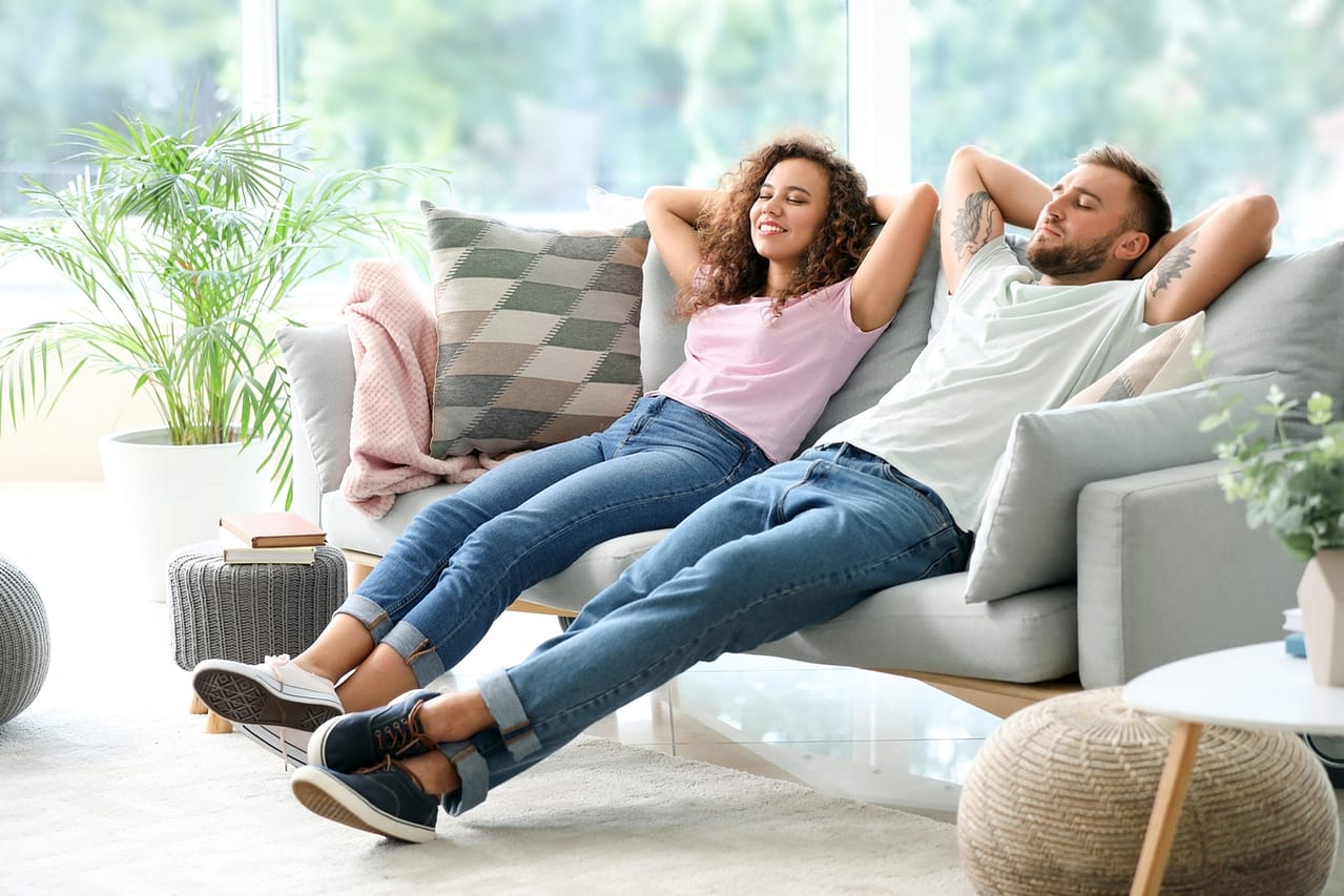 Zusammenziehen mit dem Partner in der Beziehung: So meistert ihr den neuen Lebensabschnitt! 2 happy young couple relaxing on sofa at home